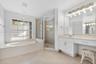 Bathroom featuring a built-in soaking tub, a tiled glass-enclosed shower, dual-basin vanity with solid-surface countertops, and large wall-mounted mir
