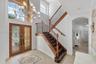 Double-height foyer featuring a dual-door entryway with decorative ironwork inserts, a large multi-tiered chandelier, tile flooring with an inlaid med