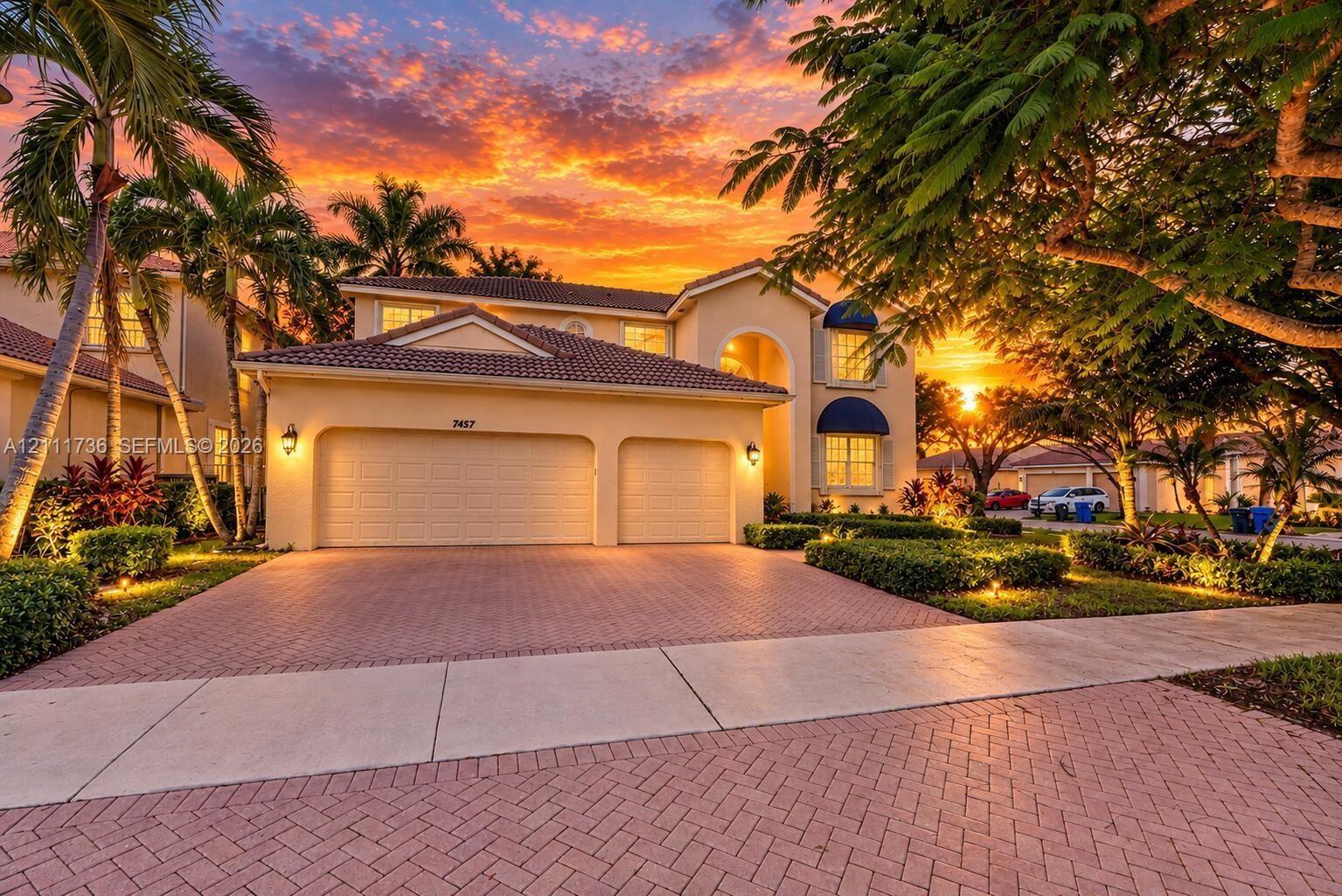 Two-story stucco exterior featuring a tiled roof, arched entryway, multi-car garage, and herringbone-patterned paver driveway