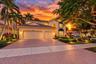 Two-story stucco exterior featuring a tiled roof, arched entryway, multi-car garage, and herringbone-patterned paver driveway