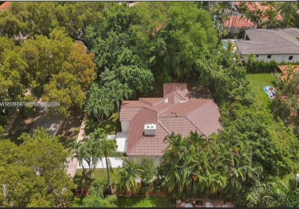 Aerial perspective featuring a multi-hipped clay tile roof, concrete driveway, and mature landscaping with extensive tree canopy