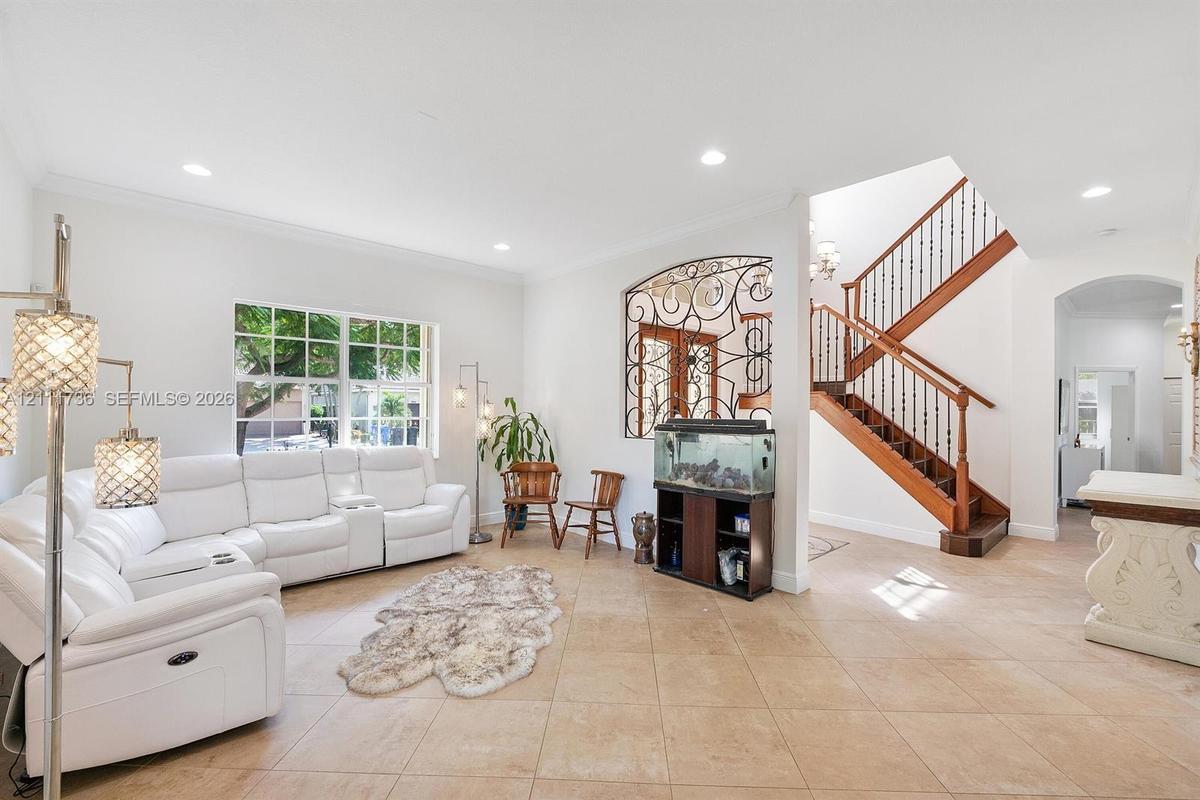 Open-concept area featuring ceramic tile flooring, recessed lighting, ornate wrought iron wall detailing, and a wood staircase with decorative baluste