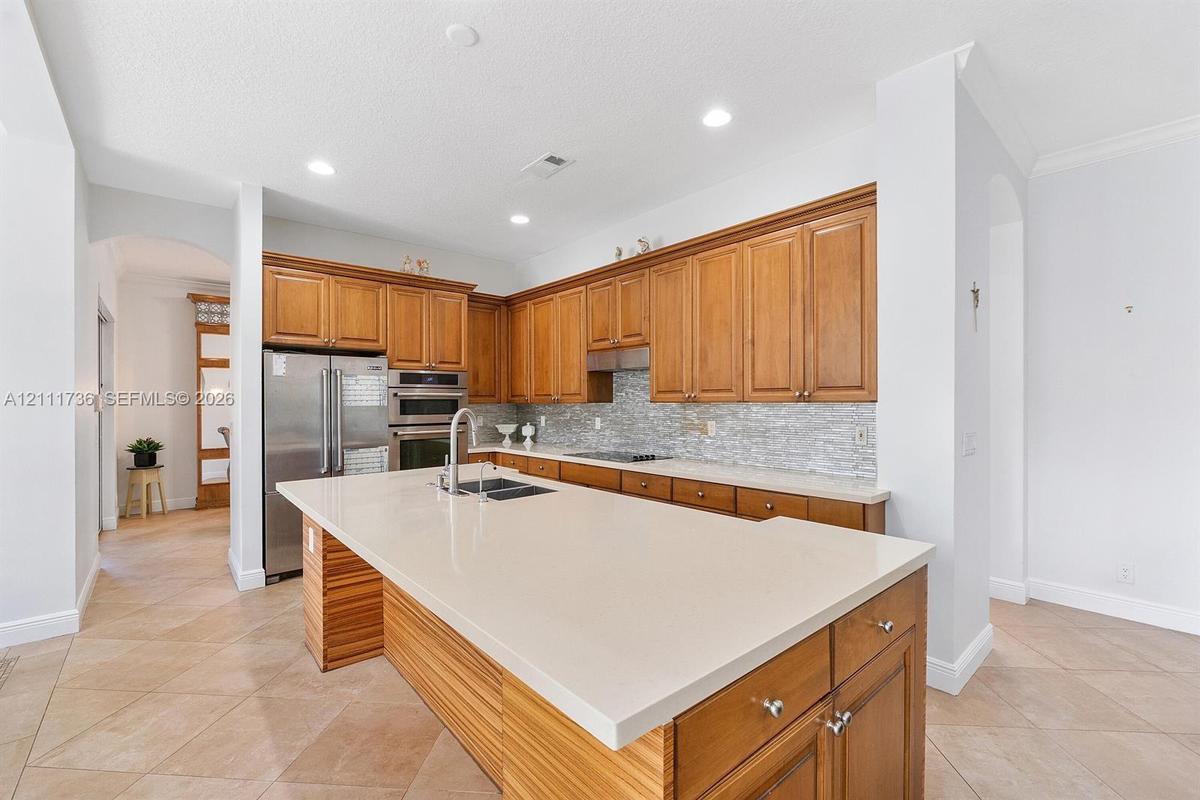 Kitchen featuring wood cabinetry, a central island with a quartz countertop, stainless steel appliances, a mosaic tile backsplash, and ceramic tile fl