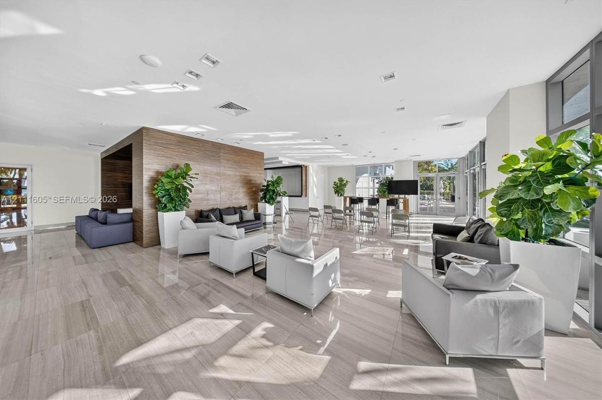 Open-plan interior featuring stone-finish flooring, floor-to-ceiling sliding glass doors, a built-in wet bar, and kitchen cabinetry with integrated ap