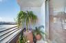 Landscaped podium terrace featuring mature tropical vegetation, a curvilinear stone-capped planter, structured white pergola, and light-toned paved ha