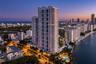High-rise architectural structure with expansive private balconies, ground-level swimming pool, and tropical landscaping situated along the waterfront