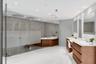 Enclosed shower with glass paneling, wood-paneled soaking tub, dual wood-finish vanity cabinets with white countertops, and integrated mirror lighting
