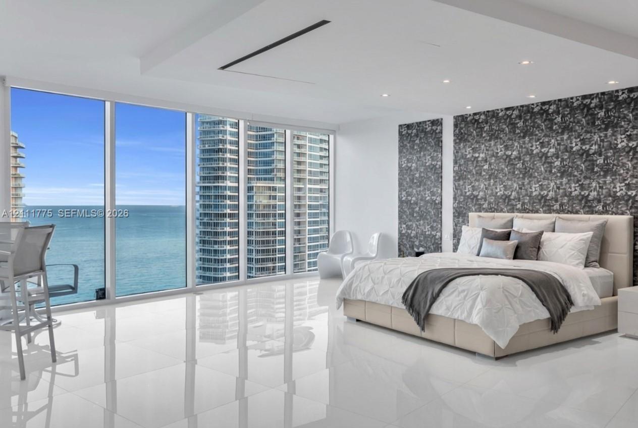 Floor-to-ceiling windows, polished stone-finish flooring, tray ceiling with recessed lighting, and patterned accent wall