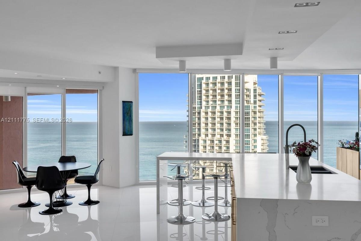 Open-concept kitchen featuring an expansive stone-surface island with integrated seating, floor-to-ceiling glass windows, recessed ceiling lighting, a