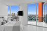 Floor-to-ceiling windows, white tile flooring, private balcony with glass railing, and wall-mounted television hardware