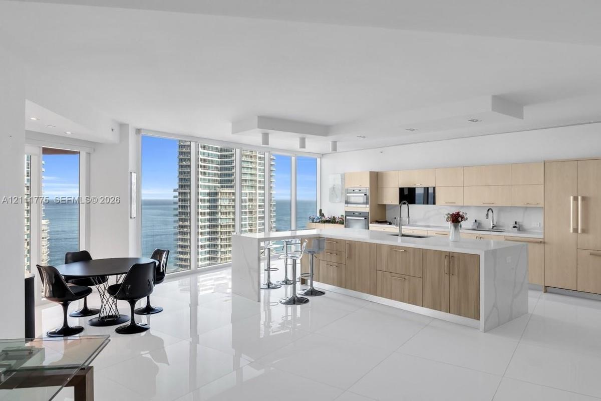 Modern kitchen featuring flat-panel cabinetry, a central island with a stone-finish waterfall countertop, polished tile flooring, and floor-to-ceiling