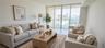 Floor-to-ceiling glass sliding doors opening to a private balcony, neutral tile flooring, and expansive water and city skyline outlooks