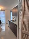 Kitchen featuring flat-panel wood-finish cabinetry, light-toned stone-surface countertops, dual-basin under-mount sink with pull-down faucet, porcelai
