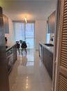 Galley-style kitchen featuring flat-panel cabinetry, light-toned stone countertops, polished tile flooring, and stainless steel built-in appliances
