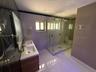 Double vanity with stone countertop and brass-finish fixtures, glass-enclosed walk-in shower with dual rainfall showerheads, and large-format tile flo