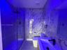 Full-height stone-patterned wall surfacing, walk-in glass-enclosed shower with rainfall showerhead, floating vanity, rectangular vessel sink, and matt
