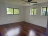 Neutral-toned room featuring dark wood-finish flooring, three black-framed windows, a ceiling fan with integrated lighting, and a wall-mounted ductles