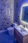 Stone-patterned wall surfacing, floating vanity with integrated rectangular sink, wall-mounted faucet, illuminated mirror, and large-format floor tili
