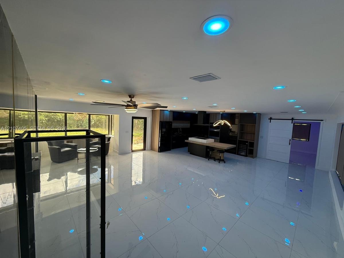 Open concept interior featuring polished tile flooring, recessed smart lighting, a kitchen island with integrated wood-finish breakfast bar, floor-to-