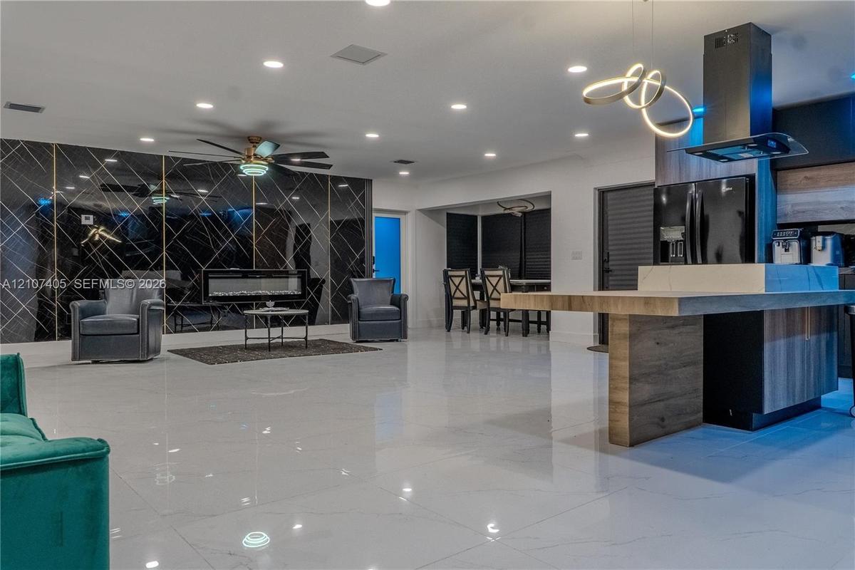 Large-format tile flooring, mirrored feature wall with built-in electric fireplace, recessed lighting, sculptural pendant light fixture, and kitchen i