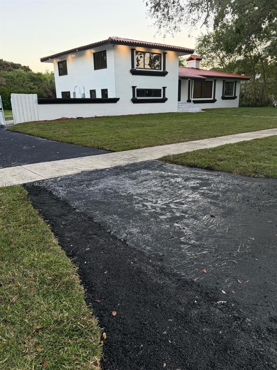 Two-story residence featuring white exterior walls with black trim, a tile roof, an attached privacy wall, and asphalt driveway