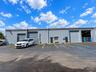 Single-story industrial exterior featuring a smooth gray concrete facade, three metal roll-up doors, two dedicated entry points, and an asphalt-paved 