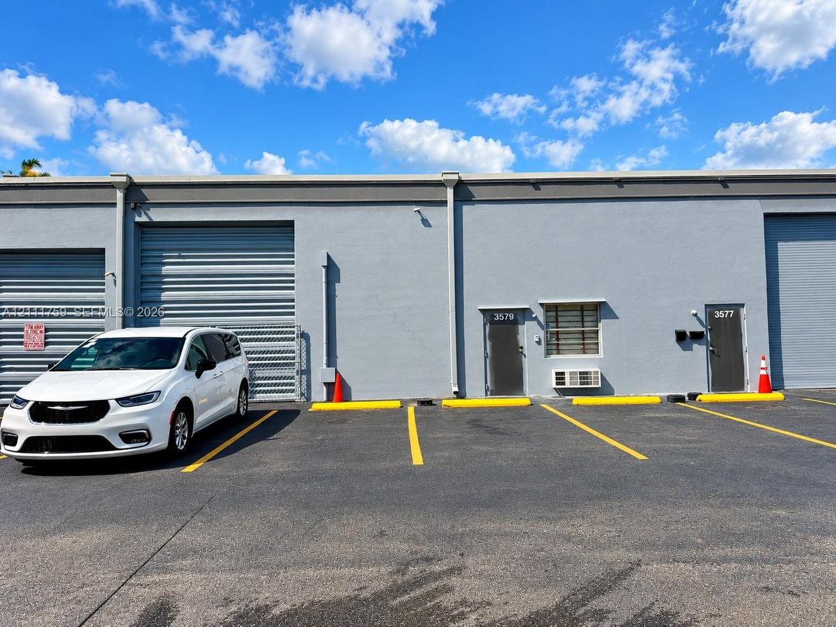 Exterior commercial facade featuring gray concrete construction, multiple metal roll-up bay doors, individual pedestrian entry doors, and dedicated as