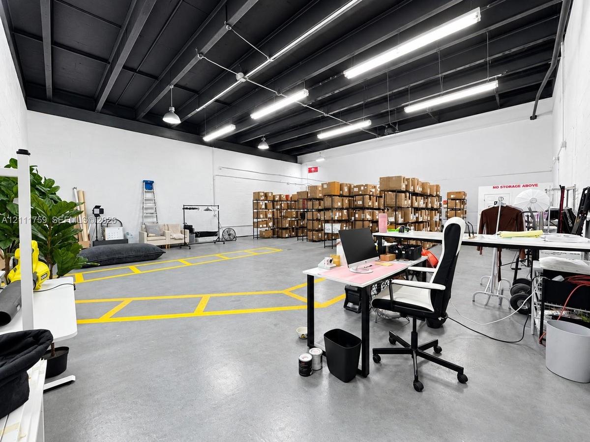 Open-concept industrial space featuring exposed beam ceilings, finished concrete flooring, painted masonry walls, and linear fluorescent lighting