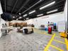 Industrial warehouse space featuring exposed black steel ceiling beams, high-output linear LED lighting, concrete flooring with painted safety demarca