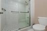 Primary Bathroom. Walk-in shower featuring large-format stone-look wall tiling, a mosaic tile floor, glass sliding doors, and chrome fixtures