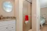 White cabinetry vanity with stone-finish countertop, undermount sink, circular wall-mounted mirror, and glass-enclosed shower