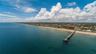 Aerial perspective of coastal landscape featuring an expansive sandy shoreline and extended deep-water pier