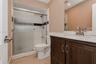 Bathroom featuring a dark wood vanity with a stone-finish countertop, undermount sink, shower with sliding glass doors, and a frameless wall mirror