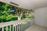 Covered balcony featuring tile flooring, textured stucco wall, and wooden balustrade railing, overlooking mature trees and golf course