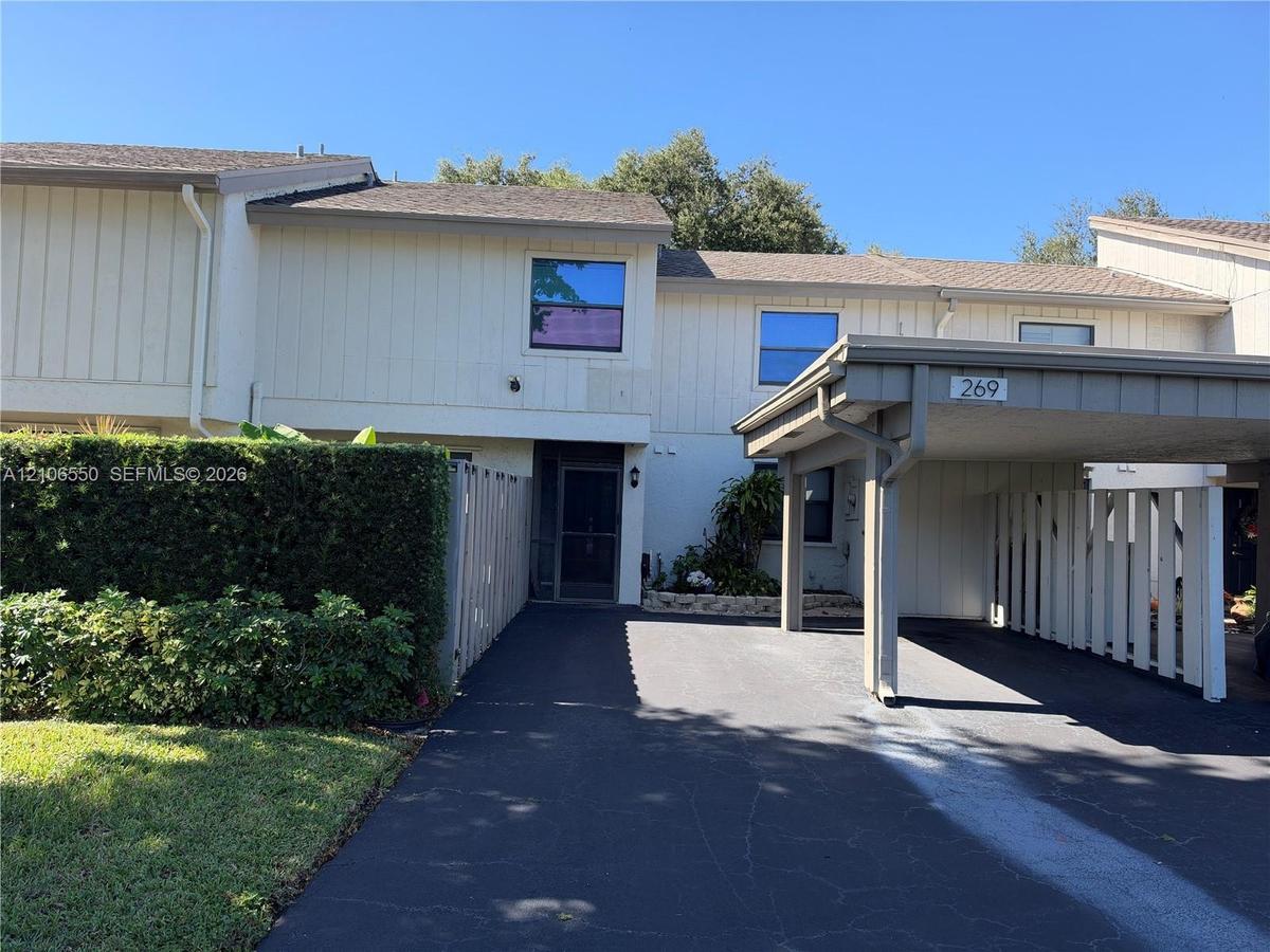 Multi-level townhouse exterior featuring vertical siding, an attached covered carport, asphalt driveway, and privacy fencing