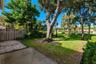 Backyard featuring a concrete patio, gravel border, vertical wood-slat privacy fencing, mature trees, and landscaped grass area