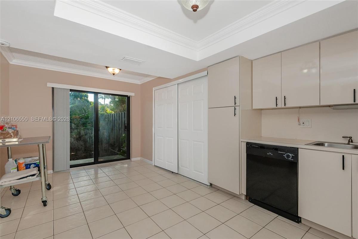 Kitchen featuring gloss-finish cabinetry, built-in dishwasher, integrated sink, tile flooring, and sliding glass doors with tray ceiling detail. large