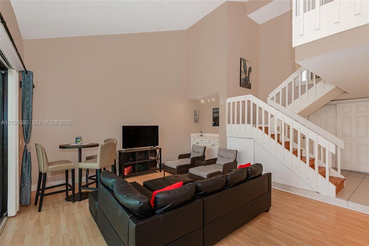 Living area featuring vaulted ceilings, wood-finish flooring, a built-in wet bar, and a wooden staircase with white balusters