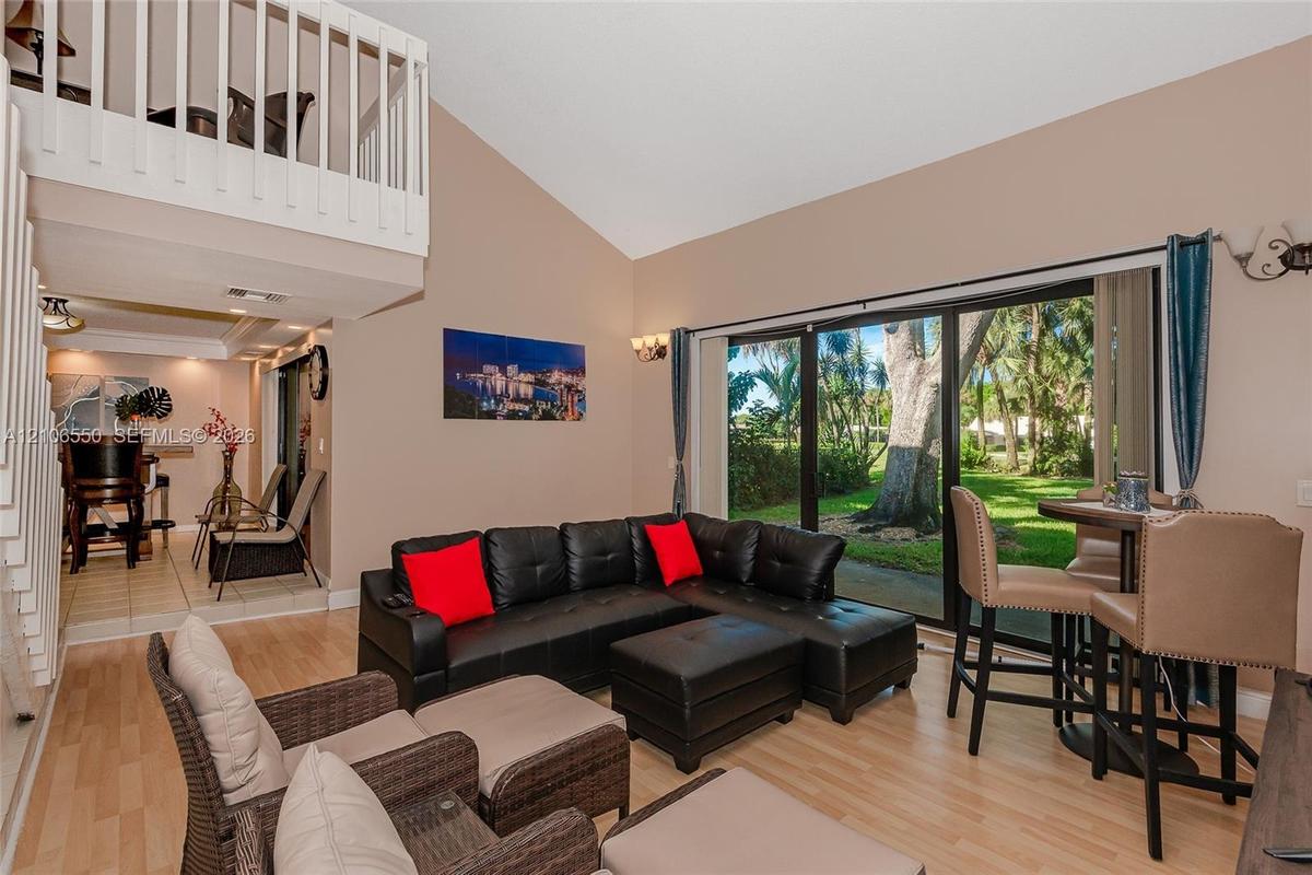 Vaulted ceiling, wood-finish flooring, white railing mezzanine, and floor-to-ceiling glass sliding doors