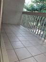 Covered balcony featuring neutral ceramic tile flooring, textured wall finish, and a slatted railing