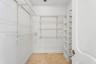 Storage area featuring stone tile flooring, white vertical built-in shelving, and adjustable metal wire rack shelving