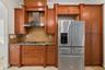 Custom wood cabinetry, stainless steel range hood, stone countertop, tiled backsplash, and stainless steel refrigerator