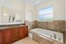 Dual-sink vanity with stone countertop, soaking tub with jetted features, full-height stone tile surround, built-in recessed wall niche, and decorativ