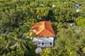 Two-story residence featuring a terracotta-tiled roof, white exterior stucco finish, and an integrated swimming pool situated within a heavily wooded 