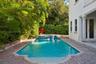 Outdoor swimming pool with a spillover spa, brick paver decking, decorative columns, and mature perimeter landscaping