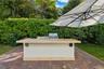 Outdoor kitchen featuring a stone-topped island, stainless steel grill, built-in speakers, and brick paver patio