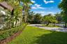 Paver driveway featuring manicured lawn, established shrubbery, mature palm trees, and perimeter fencing