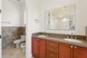Dual-sink vanity with stone countertop and cabinetry, decorative sunburst-style wall mirror, stone tile wainscoting, and ceramic flooring
