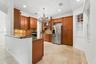 Kitchen featuring wood cabinetry, stone countertops, stone flooring, stainless steel appliances, and a chandelier