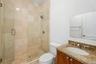 Walk-in shower featuring glass enclosure, stone tile wall surround, and stone tile flooring, accented by a vanity with stone countertop and an oval dr